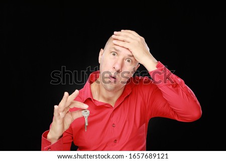 Very excited adult caucasian man in red shirt holding keys for house isolated on black background