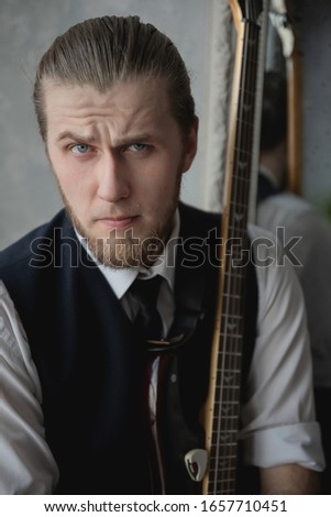 man in a white shirt and vest sits on a sofa with a guitar