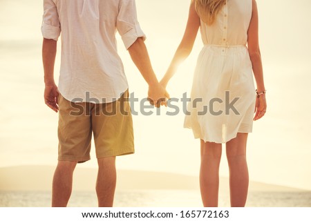 Young couple in love, Attractive man and woman enjoying romantic evening on the beach, Holding hands watching the sunset Royalty-Free Stock Photo #165772163