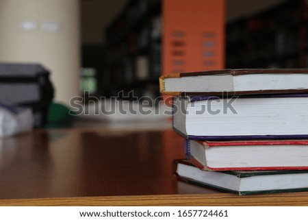 A pile of books on the table in the University Library. A piles of literature text academic archive on reading desk and aisle of bookshelves in library  background. 