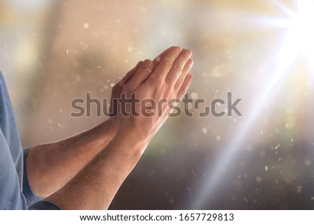 Man praying in church with hands with palms facing and flash of light. Horizontal composition