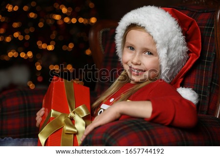 Cute little child with Christmas gift sitting in armchair at home