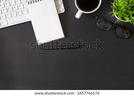 Workplace office with dark black desk. Top view from above of keyboard with notepad and coffee cup. Space for modern creative work of designer. Flat lay with copy space. Business and  finance concept.