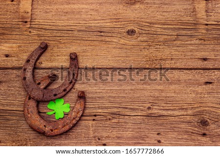 Two cast iron metal horse horseshoes, felt clove leaf. Good luck symbol, St.Patrick's Day concept. Old wooden background, horse accessories, top view