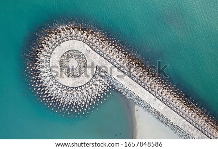 Top down view of a q-shaped jetty, reinforced with tetrapods (concrete wave breaker blocks), extruding into the turquoise sea water to protect the coast from erosion, on Yuguang Island, Tainan, Taiwan