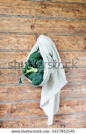 Stack, bunch with broccoli tied up in a towel cloth against a wooden wall, minimalist alternative food styling