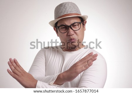 Portrait of young funy angry Asian man shows crossed arms gesture, giving warn to stop gesture, rejection concept