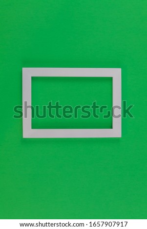White photo frame on medium green paper background for Spring, Easter, St Patrick's Day.  Flat lay, top view, copy space, portrait.