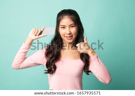 Young Asian woman thumbs up with a blank card on cyan background