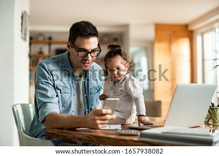 Young working father text messaging on mobile phone while being with his small daughter at home.  Royalty-Free Stock Photo #1657938082