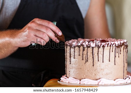 close up of a chefs hands adding melted dark chocolate lines dripping down the sides of a birthday cake