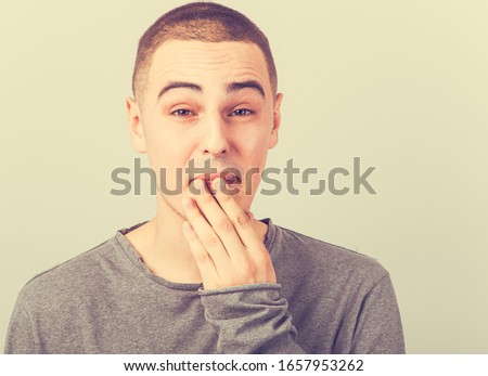 Tired fun grimacing teen guy wanting to sleep and  yawning , closing mouth the hand on toned color vintage background. Closeup portrait