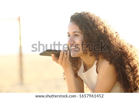 Happy latin young woman using voice recognition system on her smart phone on the beach