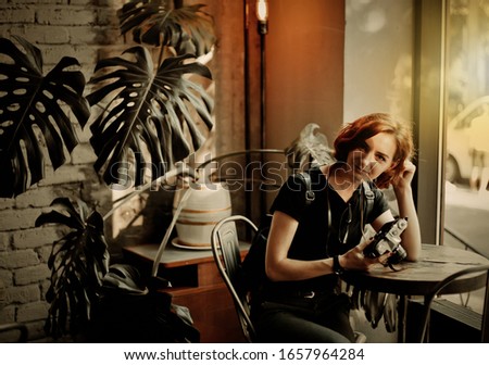 Young hipster woman holds retro camera in her hands and look at camera in old cafe