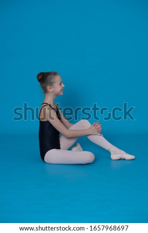 a little girl ballerina is engaged in ballet in a black swimsuit and white leggings