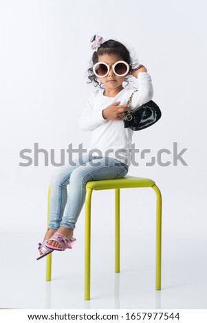 Young beautiful girl with sunglasses posing her hand bag or purse while sitting on a green stool chair. Beautiful young girl modeling her hand bag. 