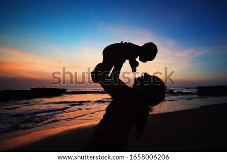 Happy family black silhouette on sunset sky background. Young mother, baby son have fun together, walk by sea beach. Mom toss and catch child. Travel lifestyle, parents with kids on summer holidays.