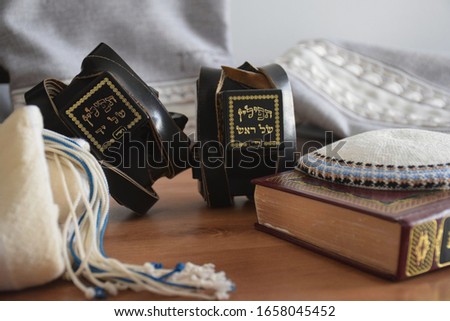 Black Tefillin (Judaica item using for the famous jewish prayer "Shema Israel" - hear us our lord, made from leather), the Jewish bible book and white 'Kippah' (skullcap) and a bag for the Tefillin. Royalty-Free Stock Photo #1658045452