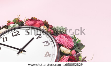 Part of big analogue plain wall clock in full bloom flowers on candy pink background. Close up with copy space, time management concept. Daylight saving time. Spring or wedding. Womens day picnic