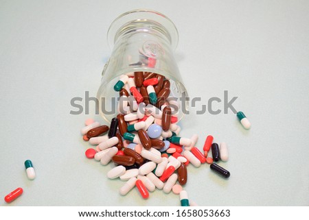 Many drug and pill spilled out of a glass on light background. Rational drug use and polypharmacy concept.  Colored Pharmaceutical  medicine capsules.