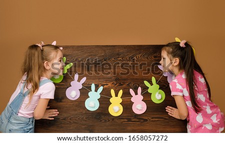 two happy little child girls holding wood board with paper bunny. Easter day. copy space