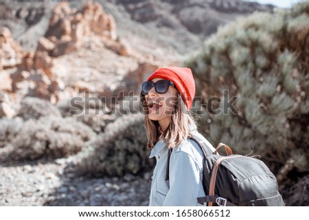 Lifestyle portrait of a stylish carefree woman dressed casually in jeans and red hat enjoying travel on the rocky terrain on a sunny day