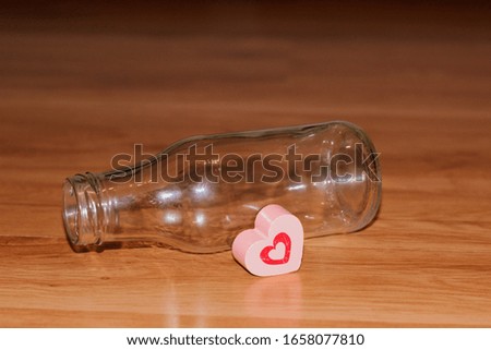 A red heart shape next to an empty glass bottle lying on boards.
