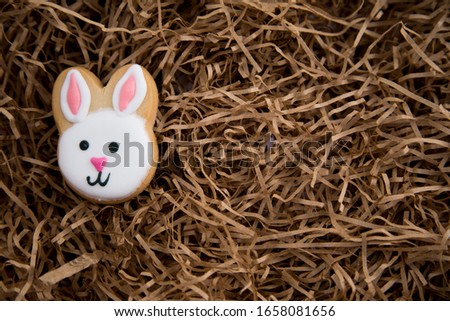 Single home cooked and decorated Easter bunny cookie.  Icing pink, white and black in the shape of rabbit heads. Sitting on brown recycled paper straw. Sustainability, homemade look. Low waste Easter
