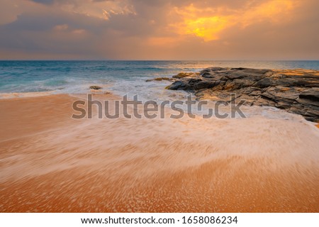 Beautiful sandy ocean beach coast with stones and rocks under beautiful sunset sky with clouds on Sri Lanka island.