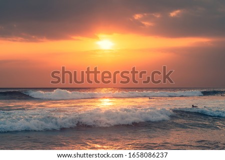 Ocean waves under beautiful sunset sky. Surfers floating on waves in expectation.