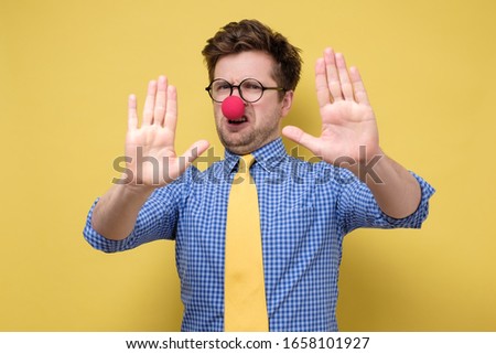 Funny caucasian man with red clown nose over isolated yellow background making stop gesture. First April concept