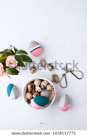 Flat lay composition of naturally-dyed quail egg and color Easter eggs lying in tray on wihte table background with feather and pink roses. Space for text