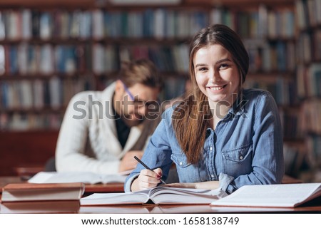 Attractive girl sitting at desk and taking notes at library