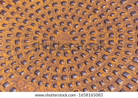 Close-up and select focus on the center of metal, rusty, round manhole with polished elements. Abstract background texture.