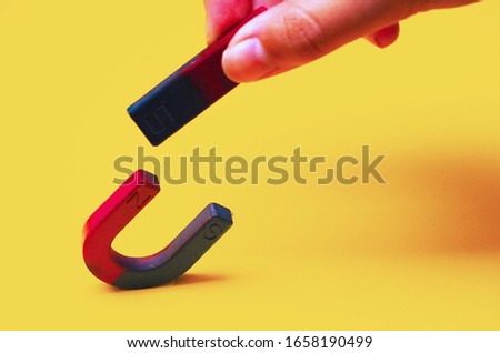 Close up of female hand holding bar magnet    Attracting horseshoe magnets