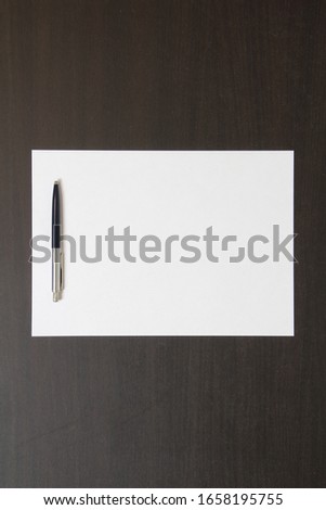 Template of white paper with pen on dark wenge color wooden background. Concept of business plan and strategy. Stock photo with empty space for text and design.