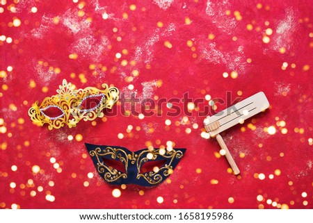 Red carnival bakground. Carnival mask and wooden gragger on bright red background. Flat lay of Purim Carnival celebration concept. Top view, copy space for text.