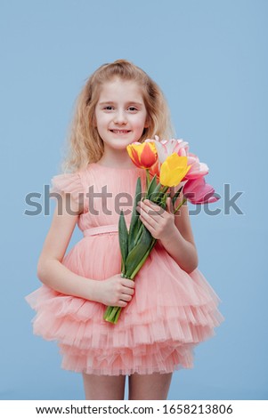 tulips. little girl with spring flowers in her hand, in pink dress, isolated on blue background in studio