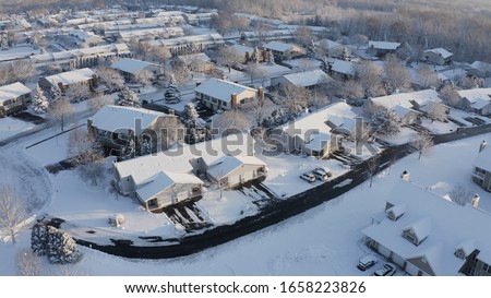 Aerial view of residential houses covered snow at winter season. Establishing shot of american neighborhood, suburb.  Real estate, drone shots, sunny morning, sunlight, from above. 