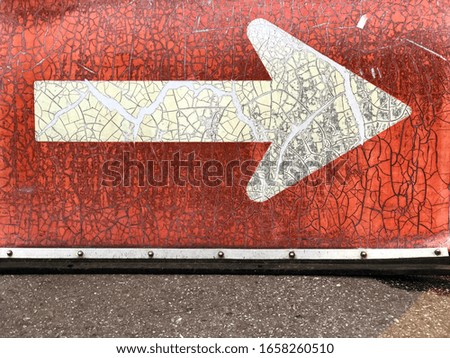 Old Arrow sign direction put on asphalt road. Painted peeling yellow arrow direction on red background.