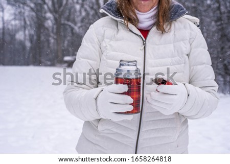 woman in winter coat holding a thermos outside on a snowy winter day
