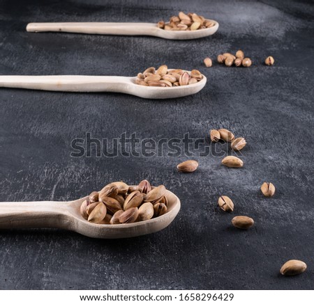 Side view pistachios in wooden spoons on dark texture background