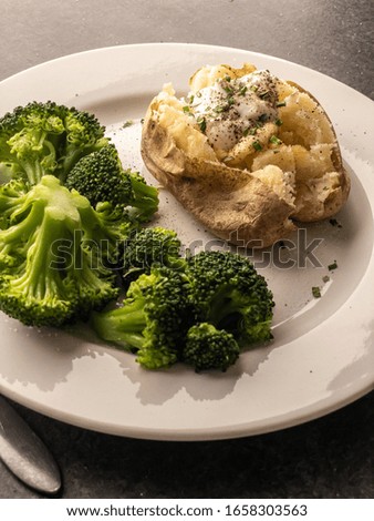 Baked potato topped with butter, Greek yogurt, and chives served with steamed broccoli on a concrete background