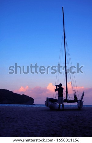 Men enjoying photography with camera near a sailboat on the beach in the evening after sunset.