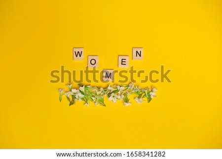 Top view woman spelled in wooden blocks on yellow bee background with flowers beneath them. Love, 8 march background. Gift, greeting, compliment concept. Copy space. place for text.