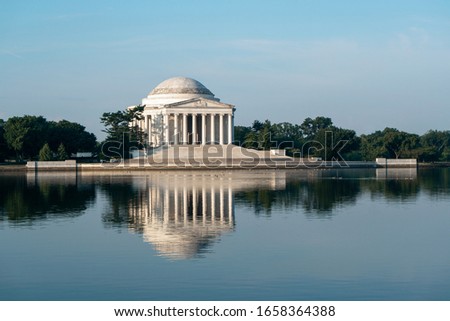 Jefferson Memorial in Washington DC at sunrise during a beautiful summer morning under a blue sky reflecting off the Tidal Basin. 
