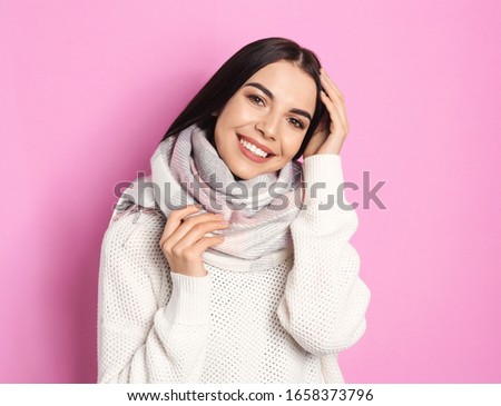Young woman wearing warm sweater and scarf on pink background. Winter season