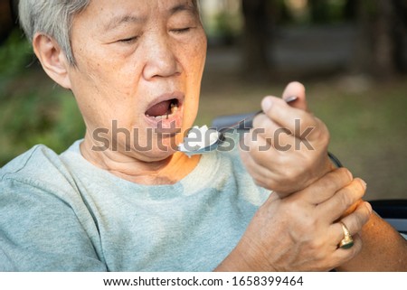 Asian senior woman holding spoon and hands tremor while eating rice,cause of hands shaking include parkinson's disease,stroke, brain injury,symptom of essential tremor,health problem of elderly people