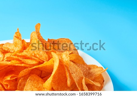 Full white ceramic plate of potato chips on blue background. Space for text