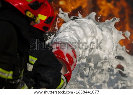 Firefighter puts out a fire. Silhouettes of firefighters with hoses with foam on a background of fire.